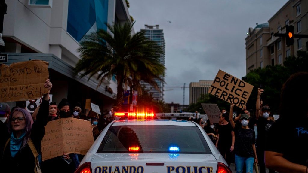 Image of police car driving through crowd of protestors against police brutality