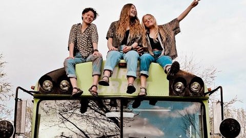 Three young woman sitting ontop of the green bus they renovated