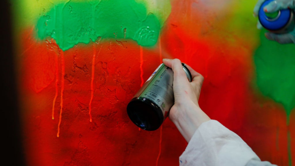 Hand holding spray paint can with multicolored wall behind