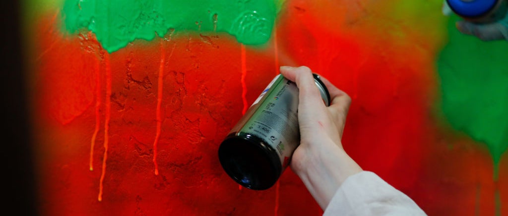 Hand holding spray paint can with multicolored wall behind
