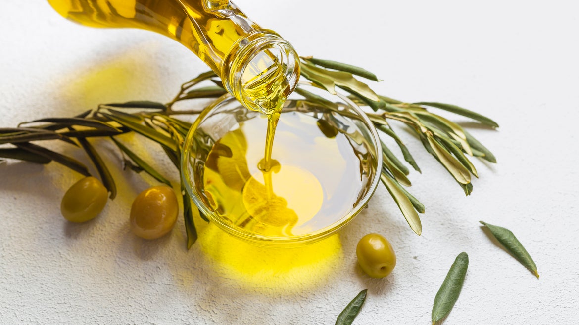 Jar of olive oil and olive branches on white background
