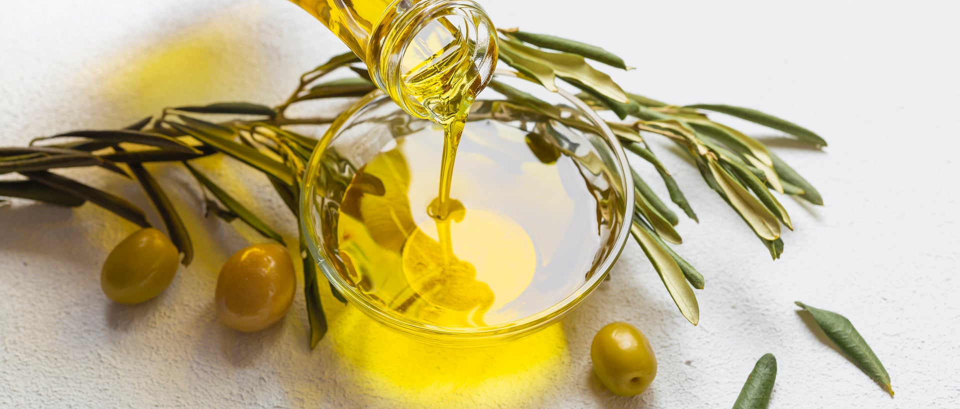 Jar of olive oil and olive branches on white background