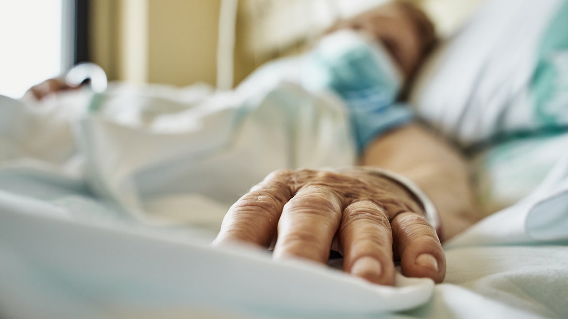 Blurred out body in mask with hand outstretched on a hospital bed