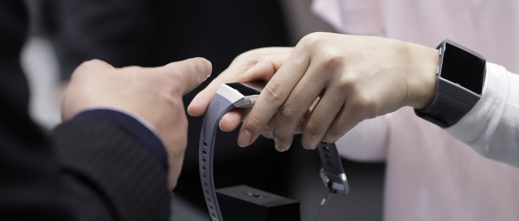 A Fitbit on a wrist with the wearer holding another