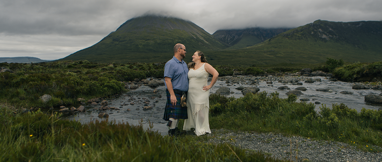 wedding photo of Amanda and Paul standing on a trail around greenery and mountains in the background