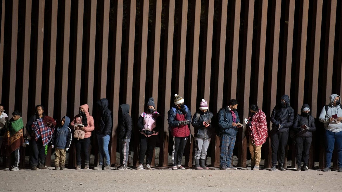 Asylum-seekers line up to be processed by US Customs and Border Patrol agents at a gap in the US-Mexico border fence near Somerton, Arizona