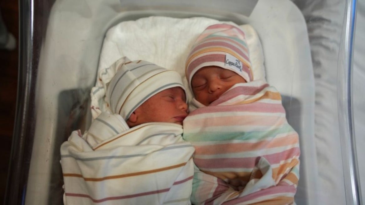 newborn twins both wearing hats and each of them wrapped in a blanket