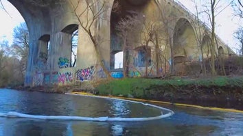 River with boom under graffitied overpass. 
