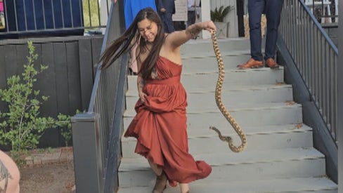 Woman in orange dress holds snake in hand