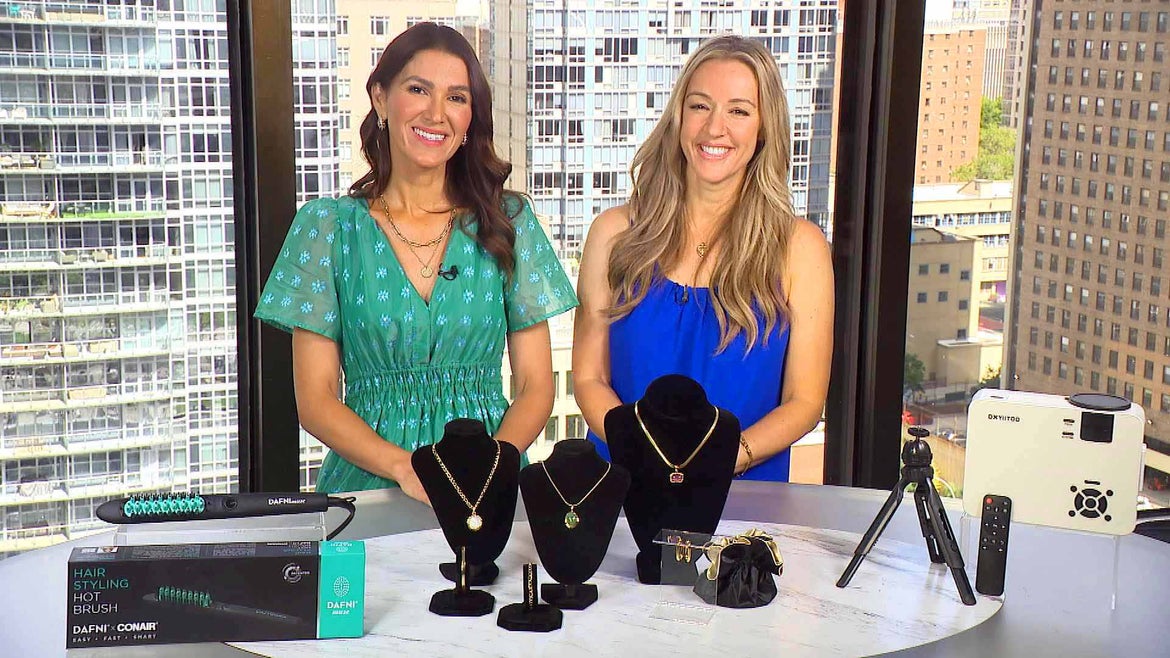 Two women standing behind a table displaying a Hot Brush, Gemstone Set, Movie Projector