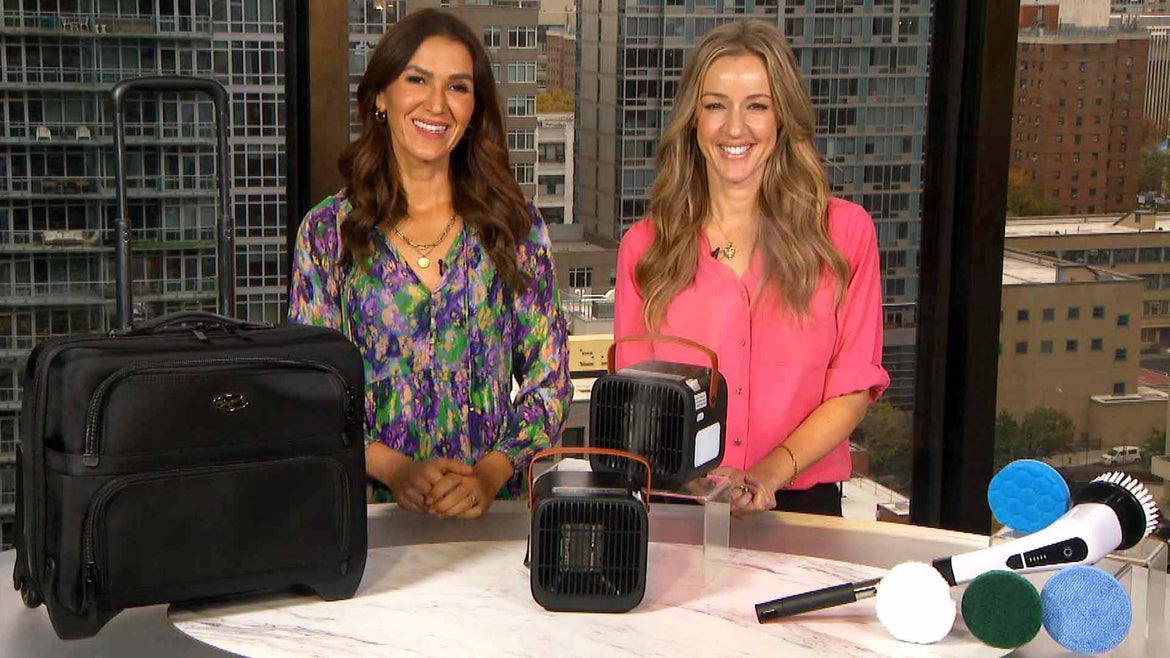 Two women standing behind a table displaying an Overnighter Bag, TheraMist Space Heaters, Electric Scrubber Brush
