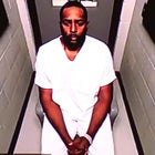 Sherrone Moore in a white jumpsuit wearing cuff as he appears virtually for court