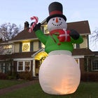 Large inflatable snowman decoration standing as tall as the house behind it
