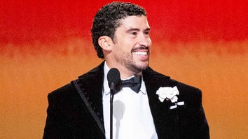 Bad Bunny smiling behind a microphone wearing a tuxedo 