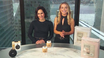 Two women standing behind a table displaying a Bluetooth Speaker, Body Creams, Sheet Set