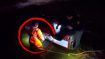 Two people next to an overturned car in water