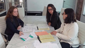 Three reporters, Katherine Kallergis, Ellen Cranley, and Sheridan Wall, sitting at a table during a meeting with paperwork on the tabletop