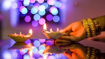 Female hand holding a Diwali lamp on the foreground of a beautifully illuminated background of colourful bokeh