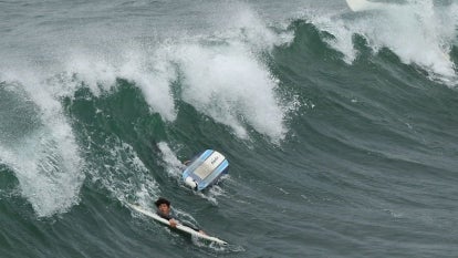 Surfers grip their surf boards in the middle of a wave in Manhattan Beach, California, on January 15, 2022. - 