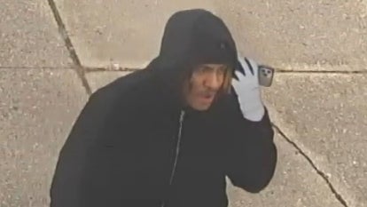 suspect wearing black hoodie and reflective gloves holding a phone to his ear