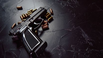 Black gun on black surface surrounded by bullets