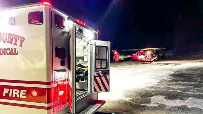 back of ambulance truck with doors open and a red helicopter in the distance that has a logo reading "REACH"
