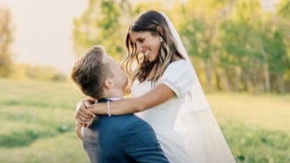 Groom holding up bride. Bride, wearing white dress, smiles and has her arms around the neck of her new husband.