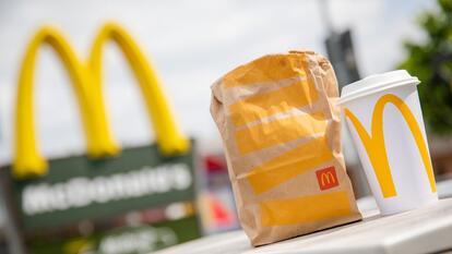 A McDonald's to-go bag and an accompanying to-go cup stand in front of a McDonald's