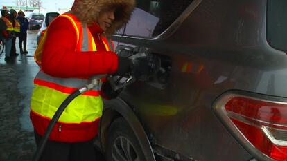 Woman with reflective vest pumping gas.