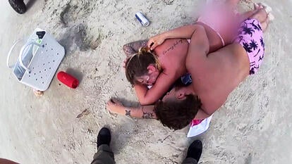 Two parents lie asleep on the beach.