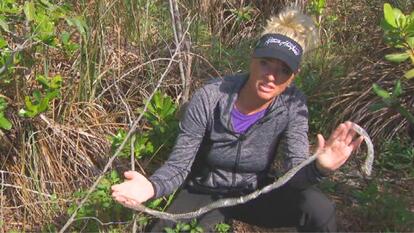 Amy Siewe crouching over grass holding shedded python skin