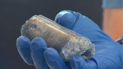 hand with blue glove holding chunk of metal