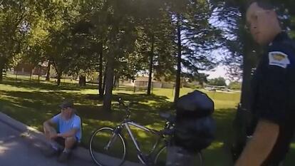 Police talking to man sitting on curb next to bicycle.