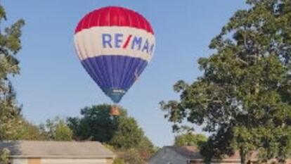 hot air balloon with Re/Max logo on it hovering over house