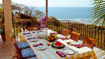 Table set for 8 on a patio with the ocean in the background