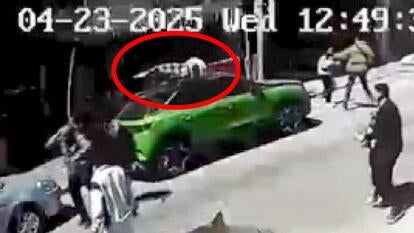 Surveillance image of a man lying on top of a green car parked on the street