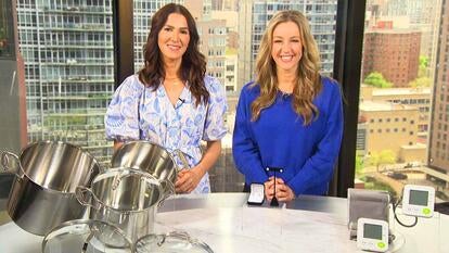 Two women standing behind a table displaying steel pots, earrings, and blood pressure monitors