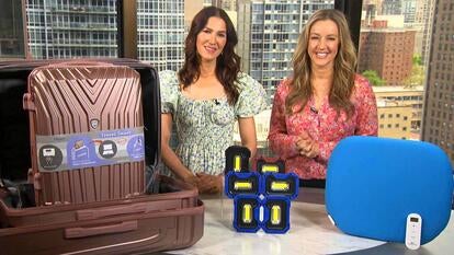 Two women behind a table displaying suitcases, work lights, and cushion