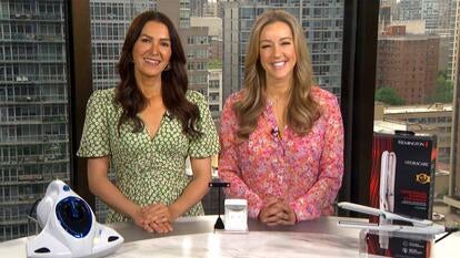 Two women standing behind a display of a vacuum cleaner, earrings, and a flat iron