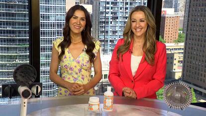 Two women behind a table displaying a hair dryer, body wash set, and a fan