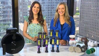 Two women behind a table displaying a robot vacuum, emergency lights, and scrub brushes