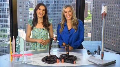 Two women standing behind a table displaying knives, hoses, and a steam mop