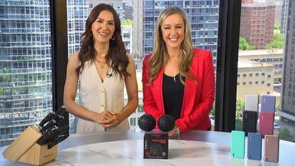 Two women standing behind a table displaying a knife set, massage balls, and powerbanks