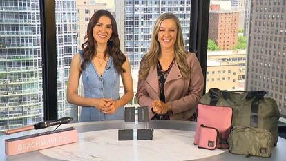 Two women standing behind a table displaying a curling iron, power banks, and duffel bags