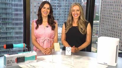  Two women standing behind a table displaying a brush, battery, and air purifier
