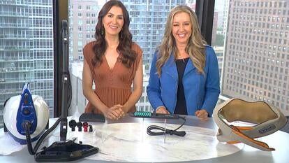 Two women standing behind a table displaying a steam cleaner, hot brush, and massager
