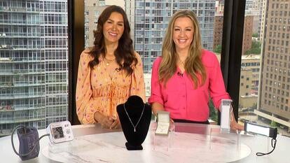 Two women standing behind a table displaying a blood pressure monitor, a necklace and powerbanks