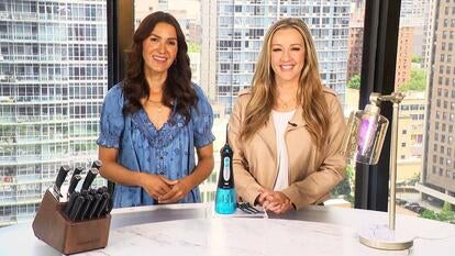 Two women standing behind a table displaying a knife set, water flosser, and lamps