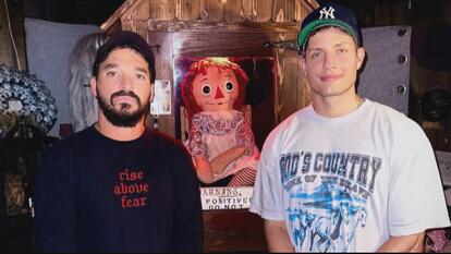 Two men, including comedian Matt Rife, standing next to the notorious Annabelle doll