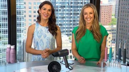 Two women standing behind a table displaying shampoo and conditioner, a hair drier and electric toothbrushes
